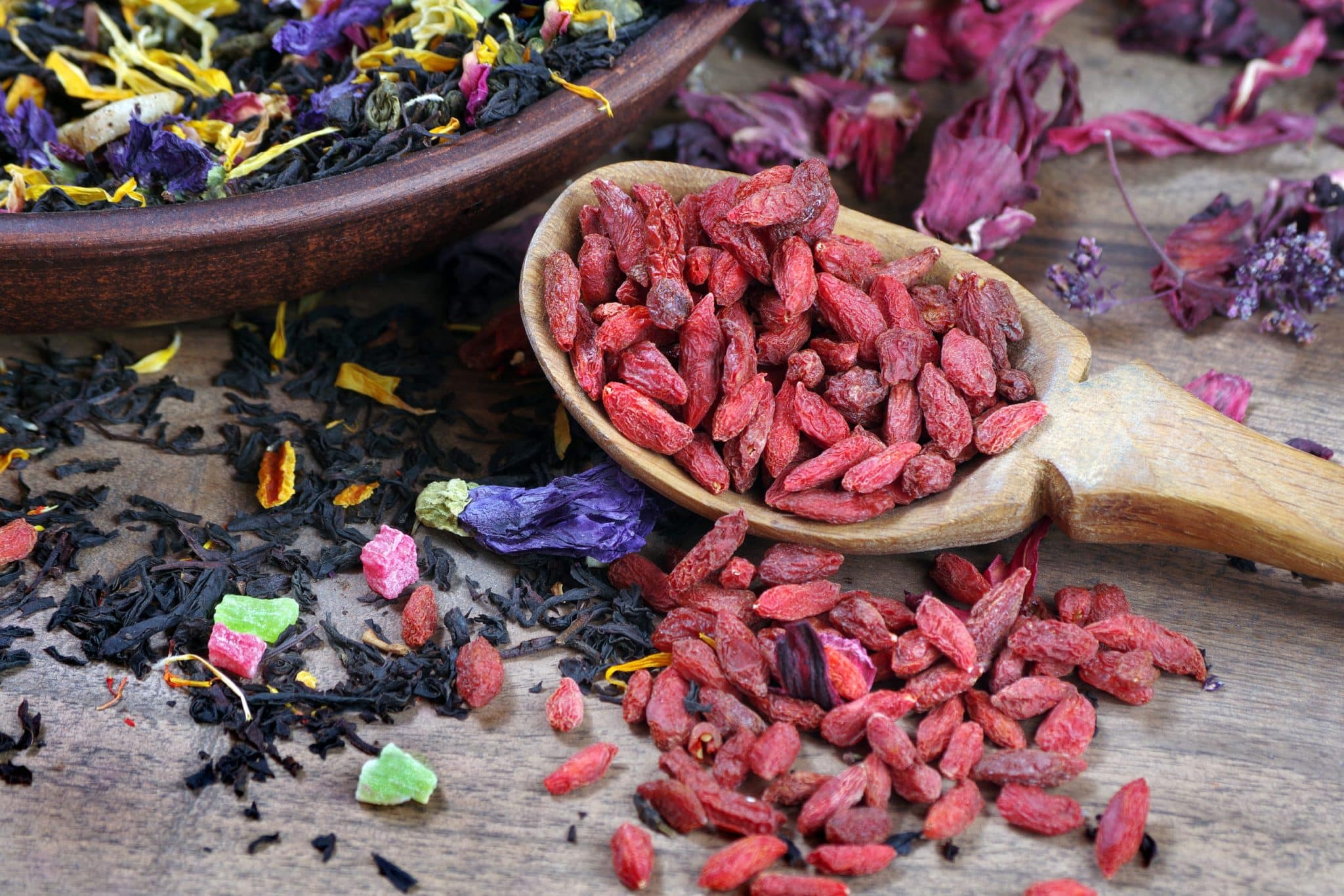 goji berries in a wooden spoon and various tea on a wooden table. blended tea with flower petals and goji berries close-up